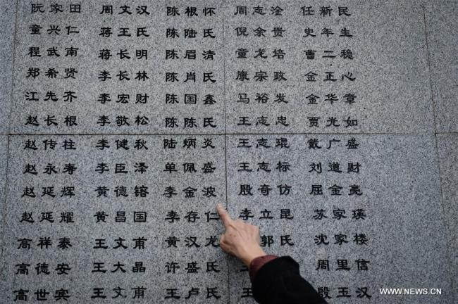 A family member of a victim in Nanjing Massacre points to a newly added name on the wall at the Memorial Hall of the Victims in Nanjing Massacre by Japanese Invaders in Nanjing, capital of east China's Jiangsu Province, Dec. 10, 2016. [Photo: Xinhua/Li Xiang]