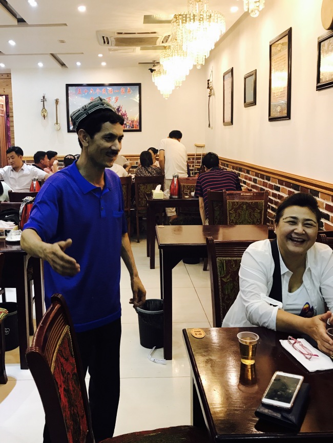 Abdulla Ulaxim is greeting his customers in his grill restaurant.[Photo: from China Plus]