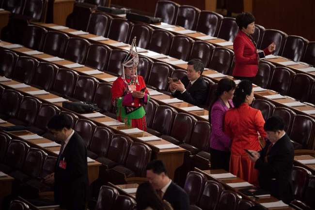 A delegate (C) wearing an ethnic minority outfit looks at her smartphone before the third plenary session of the fifth session of the 12th National People's Congress (NPC) at the Great Hall of the People in Beijing on March 12, 2017. [Photo: VCG]
