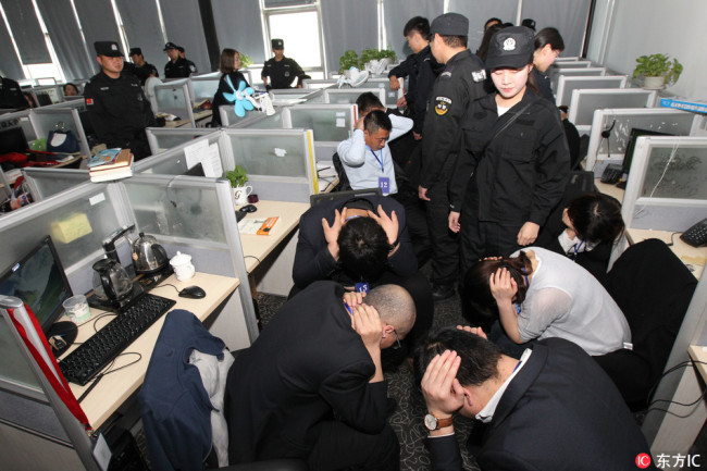 Chinese policemen detain suspects and seize fake items after breaking up a telecommunication fraud ring in Beijing, China, April 12, 2017. [Photo: IC]