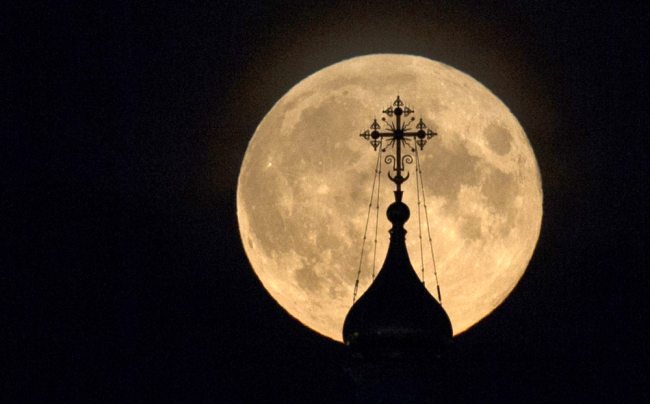 A red moon appears above a Russian Orthodox Church at Red Square in Moscow, Russia, Oct. 8, 2014. The moon appears orange, the result of sunlight scattering off the Earth's atmosphere. This is known as the blood moon. [Photo: AP/Pavel Golovkin]