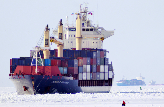The cargo vessel 'Fesco Vladimir' navigates a channel cleared by an icebreaker, as a man fishes in the frozen Gulf of Finland on March 15, 2011. [File Photo: AP/Dmitry Lovetsky]