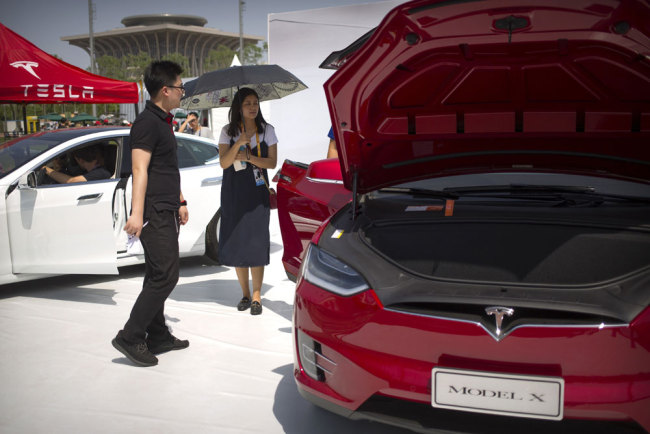 In this April 29, 2017, file photo, a visitor holds an umbrella as she looks at a Tesla Model X car on display at the G Festival, part of the Global Mobile Internet Conference (GMIC) in Beijing. [File photo: AP/Mark Schiefelbein]