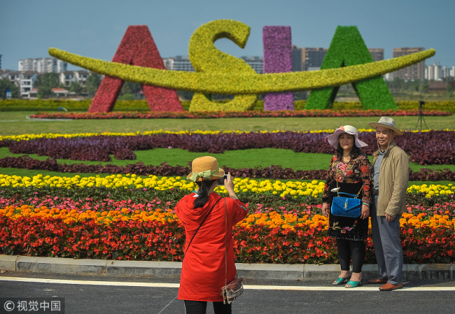 Visitors pose for photos in front of a plant statue of Boao Forum for Asia logo in Boao, Hainan Province, on March 23, 2018. [File photo: VCG]