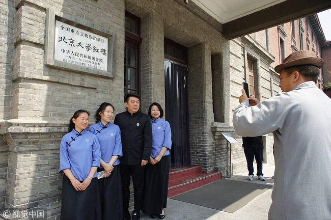 Visitors wearing the then student uniforms take pictures in front of Red Building, or Honglou. [Photo: VCG]