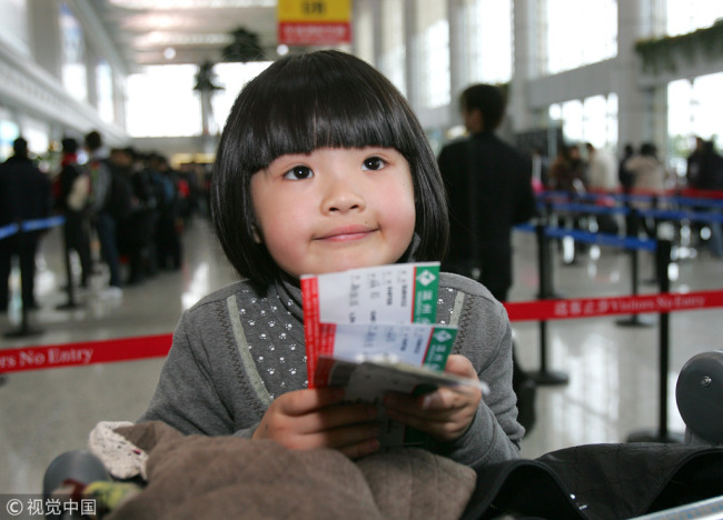 A child waits at a departure hall with three tickets in her hand, including her own child-price ticket and her parent's tickets. [File Photo: VCG]