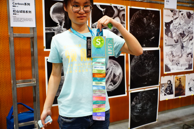 At the art gallery of the Asia-Pacific Science Fiction Convention, a volunteer showcases all the badge ribbons that she has collected.[Photo:CRI]