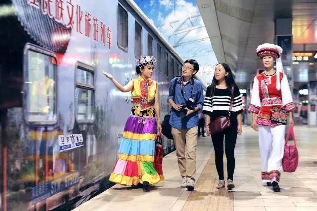 Crew members wearing ethnic outfits welcome passengers outside a tourist train linking Kunming and Lijiang in Yunnan Province. [Photo: China Railway]