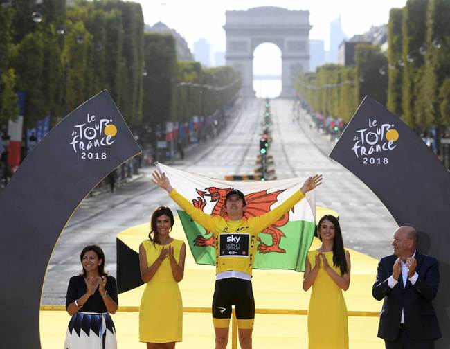 Tour de France winner Britain's Geraint Thomas, wearing the overall leader's yellow jersey, and draped in the flag of Wales celebrates on the podium in Paris, France, Sunday July 29, 2018. [Photo: Stephane Mantey, pool via AP]