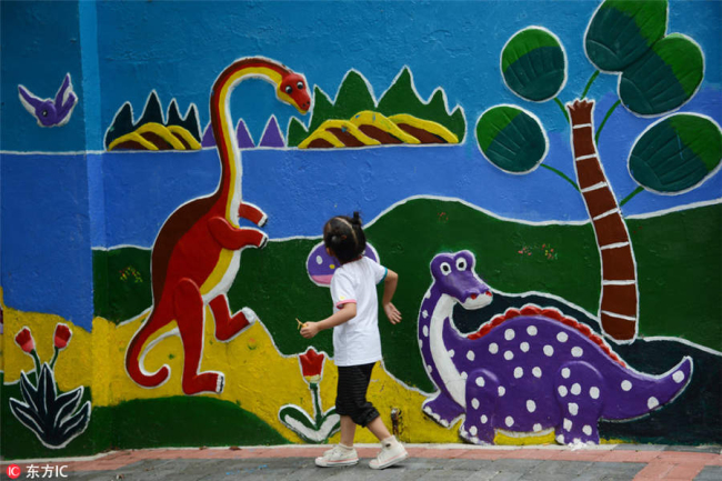 A child looks at a dinosaur street mural in Guiyang city, Southwest China's Guizhou province, July 29, 2018. [Photo/IC]
