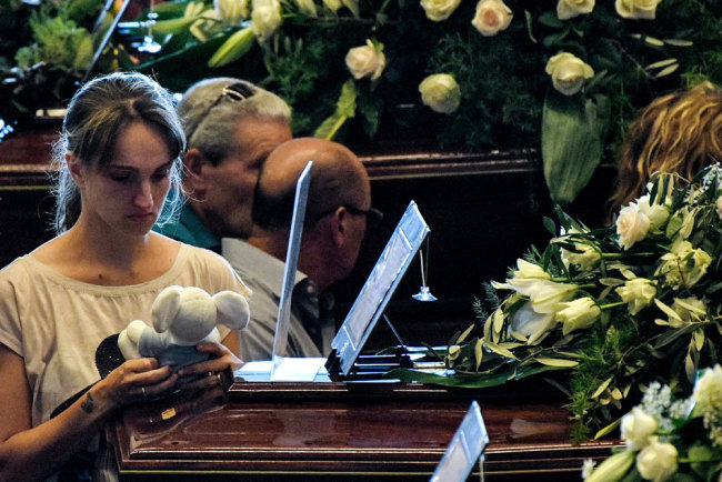 A relative holds a teddy bear as she mourns near the coffin of a victim of the collapsed Morandi highway bridge, prior to the start of the funeral service, in Genoa, on August 18, 2018. [Photo: AFP/Piero Cruciatti]