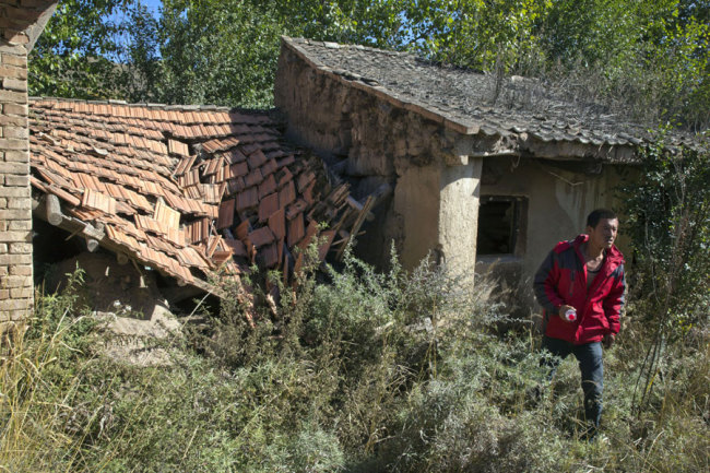 In this photo taken Oct. 9, 2015, Yang Jingrong walks through a deserted home of his neighbors who relocated from Dacha village of Xiji county in northwestern China's Ningxia Hui autonomous region. [File Photo: AP/Ng Han Guan]