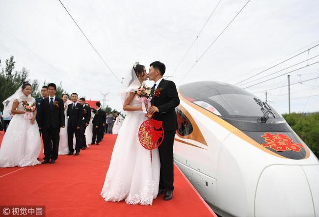 The newlyweds kiss(亲吻) in front of a Fuxing bullet train in Changchun, Jilin Province on August 18. [Photo: VCG]