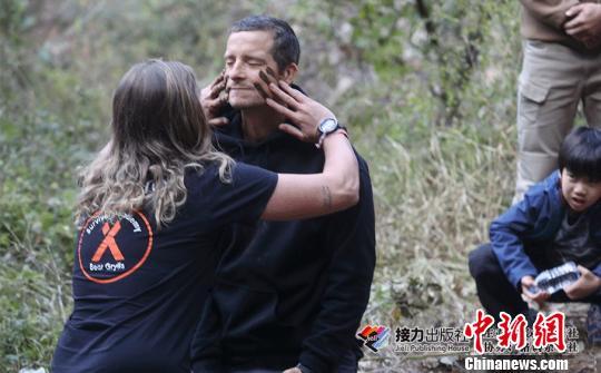 A woman puts mud on Bear Grylls' face. [Photo: Chinanews.com]