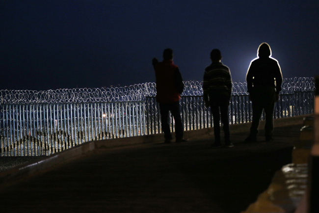 Residents stand on a hill before barriers, wrapped in concertina wire, separating Mexico and the United States, where the border meets the Pacific Ocean, in Tijuana, Mexico, Saturday, Nov. 17, 2018. [Photo: AP/Marco Ugarte]