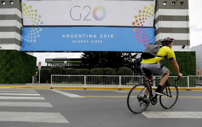 A man rides a bicycle past a banner promoting the G20 summit at the Costa Salguero Center, in Buenos Aires, Argentina, Tuesday, Nov. 27, 2018. [Photo: IC]
