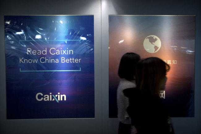 In this Jan. 18, 2018 photo, staffers walk past a billboard reading "Read Caixin - Know China Better" at the Caixin Media offices in Beijing. [Photo: AP]