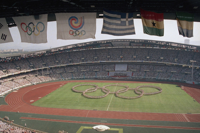 In this Sept. 17, 1988, file photo, flags frame the Olympic Stadium as participants form the Olympic rings on the field during opening ceremonies in Seoul, South Korea. Seoul hosted the Summer Olympics, and North Korea again boycotts in 1988. The two Koreas will meet at their tense border on Tuesday, Jan. 9, 2018 to discuss how to cooperate on the Olympics. [Photo: AP]