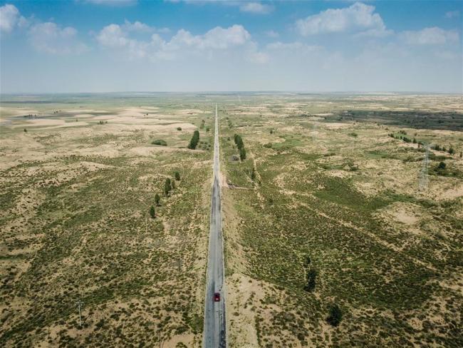 A vehicle runs on the highway S215 through the Kubuqi Desert in Hangjin Banner, Ordos City, north China's Inner Mongolia Autonomous Region, July 31, 2018. [Photo: Xinhua]