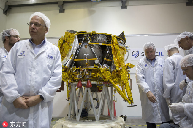 In this Monday, Dec. 17, 2018 file ., technicians stand next to the SpaceIL lunar module, an unmanned spacecraft, on display in a special clean room during a press tour of their facility near Tel Aviv, Israel. SpaceIL and the state-owned Israel Aerospace Industries plan to launch the lunar lander on a SpaceX Falcon rocket Thursday night, Feb. 21, 2019, from Cape Canaveral, Fla. [File Photo: IC]