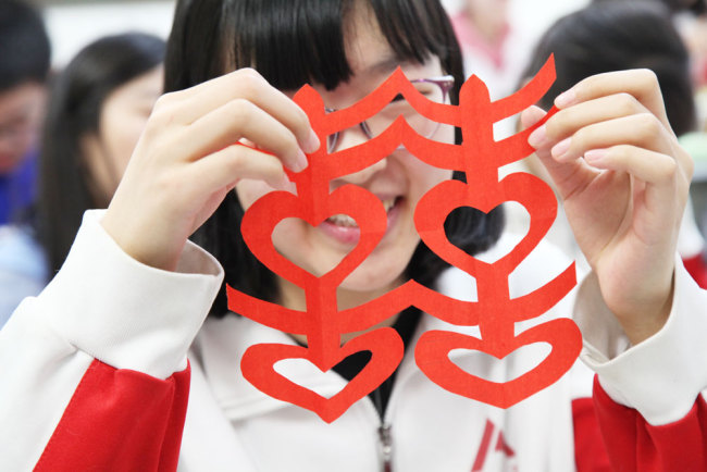 A student displays her paper-cutting of the traditional Chinese ornament design "Double Happiness" during an elective class on paper-cutting at the High School Affiliated to Renmin University of China in Beijing on Thursday, March 7, 2019. [Photo: China Plus]