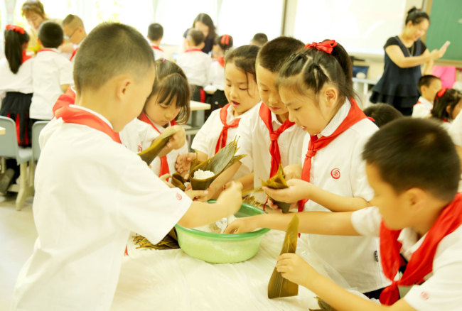 Pupils at Xiejiawan Primary School in Chongqing learn how to make zongzi, the Chinese sticky rice dumplings traditionally eaten during the Dragon Boat Festival. [Photo provided to China Plus]