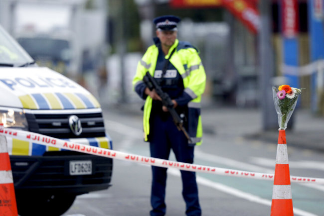 Flower rest at a road block, as a Police officer stands guard near the Linwood mosque, site of one of the mass shootings at two mosques in Christchurch, New Zealand, Saturday, March 16, 2019. [Photo: AP/Mark Baker]