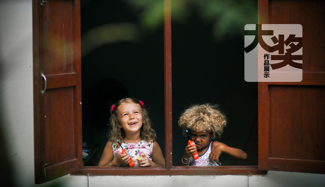 This undated photo shows a boy from France and a girl from Belarus playing together by a window in a city in Thailand. [Photo: China Plus]