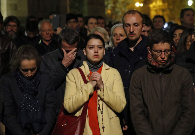 People pray as Notre Dame cathedral burns in Paris, Monday, April 15, 2019. [Photo: AP/Christophe Ena]