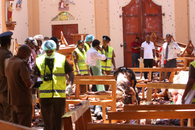 Sri Lankan security personnel walk past debris next to a dead body slumped over a bench following an explosion in St Sebastian's Church in Negombo, north of the capital Colombo, on April 21, 2019. [Photo: AFP]