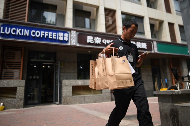 A deliveryman carrying bags of coffee walks out a Luckin Coffee in Beijing on August 2, 2018. [Photo: AFP]