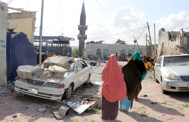 People walks past a destroyed car on the site of the explosion near the Somali parliament in the capital Mogadishu on June 15, 2019. [Photo: AFP]