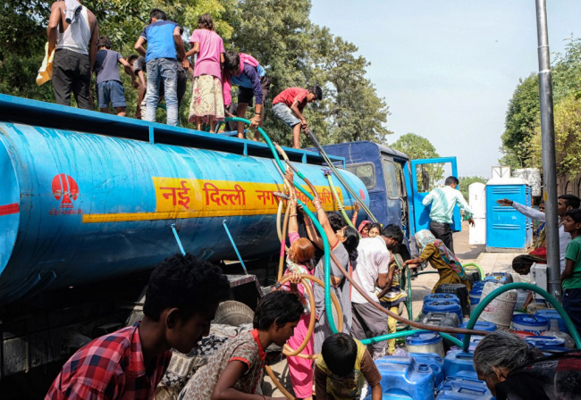 Indian residents use hoses to collect drinking water from a tanker truck during a hot summer day in the low-income neighborhood of Sanjay camp in New Delhi on June 12, 2019. [Photo: AFP/Noemi Cassanelli]