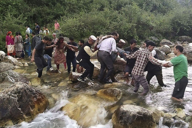 Local residents help accident survivors cross a river after a bus carrying some 50 passengers fell into a 150-metre (500-foot) gorge near Banjar, in the mountainous Kullu district of the Indian state of Himachal Pradesh on June 20, 2019. [Photo: STR / AFP]