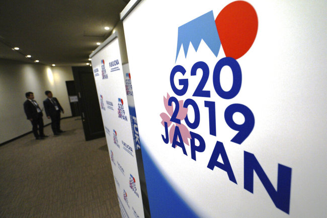 In this June 7, 2019, staff members stand near the emblem of G20 2019 Japan at the entrance of the press center of G20 Finance Ministers' and Central Bank Governors' Meeting in Fukuoka, western Japan. [File photo: AP/Eugene Hoshiko]
