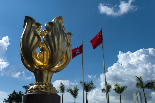 The Hong Kong flag (C) and the People's Republic of China flag (R) fly next to the statue of a golden bauhinia flower in Hong Kong, China, June 7, 2017. [File Photo: IC]