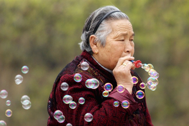 An old woman is blowing bubbles at a park, in Zhengzhou, Henan Province, on March 8, 2009. [File Photo: VCG]