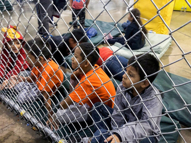 Detained children sit on pads behind cyclone fencing at the Central Processing Center in McAllen, Texas, on July 13, 2019. [Photo: IC]