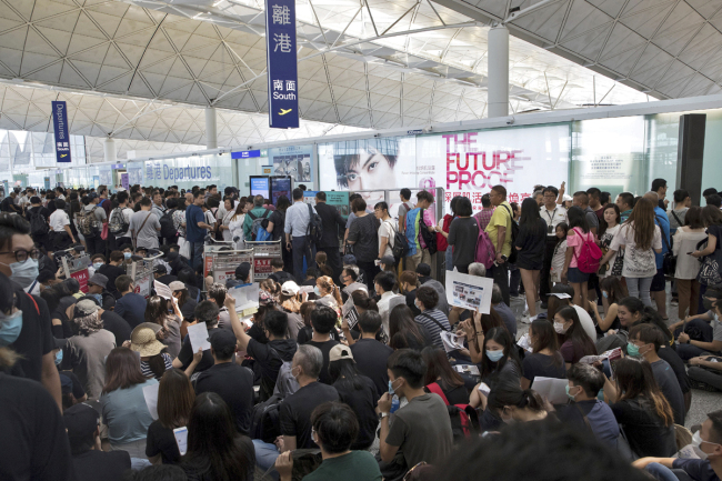 Travelers line up as protesters stage a sit-in rally near the departure gate of the Hong Kong International Airport in Hong Kong, Aug. 13, 2019. [Photo: AP/Vincent Thian]