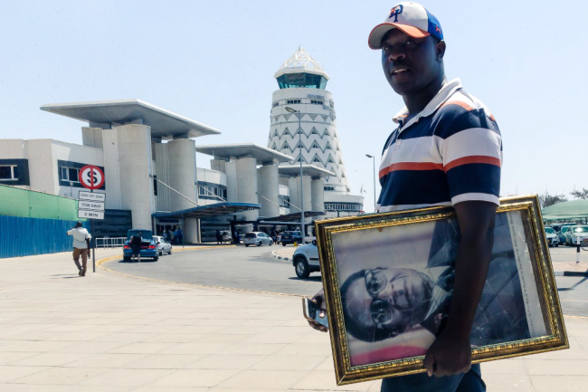 A man carrying a portrait of late former Zimbabwe president Robert Mugabe makes his way to the Robert Mugabe International Airport where the body of the deceased leader is expected today, on September 11 2019 near Harare. [Photo: AFP/Jekesai Njikizana]