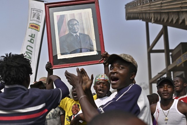 Youth carrying a portrait of Zimbabwe's late former president Robert Mugabe sing as they wait at the historic Rufaro stadium in the capital, Harare, for the arrival of his body where it will lay in state for members of the public to view on September 12, 2019. [Photo: AFP/Tony Karumba]