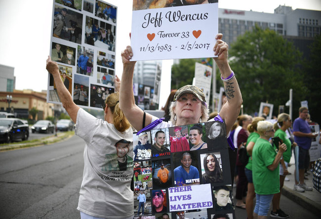 In this Aug. 17, 2018, file photo, Lynn Wencus of Wrentham, Mass., holds a sign with a picture of her son Jeff and wears a sign of others' loved ones lost to OxyContin and other opioids during a protest at Purdue Pharma LLP headquarters in Stamford, Conn. [File photo: AP]