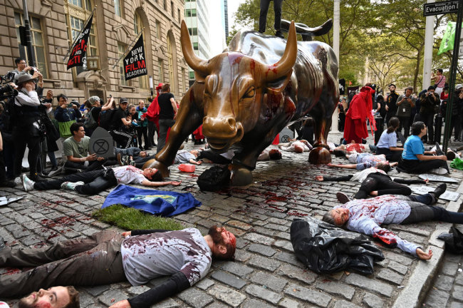 Protestors covered in fake blood gather around the Wall Street Bull during an “Extinction Rebellion” demonstration in New York on October 7,2019. [Photo: AFP]