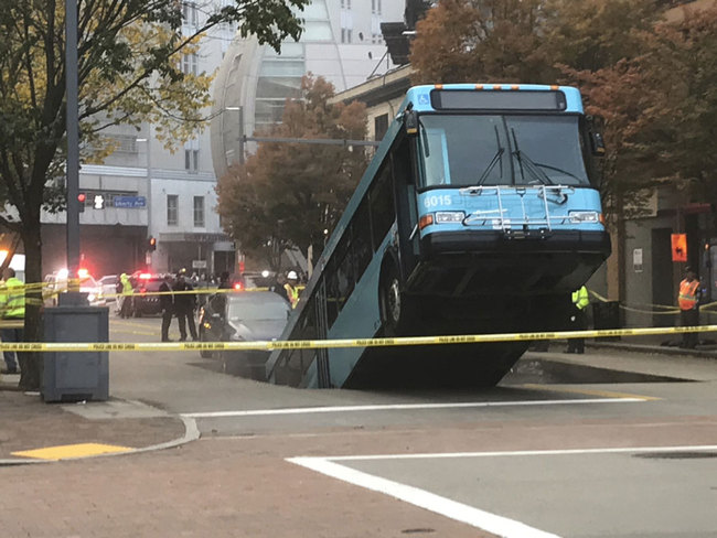 Pittsburgh police officers stand near a Port Authority bus that had fallen into a sinkhole along 10th Street and Penn Avenue in Pittsburgh on Monday, Oct. 28, 2019. The bus and a car fell in the sinkhole shortly before 8 a.m. One person was taken to the hospital for a minor injury. [Photo: Kristina Serafini/Pittsburgh Tribune-Review via AP]