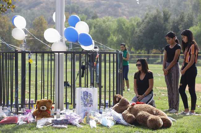 Parent Mirna Herrera kneels with her daughters Liliana, 15, and Alexandra, 16 at the Central Park memorial for the Saugus High School victims in Santa Clarita, Calif., Friday, Nov. 15, 2019. [Photo: AP/Damian Dovarganes]