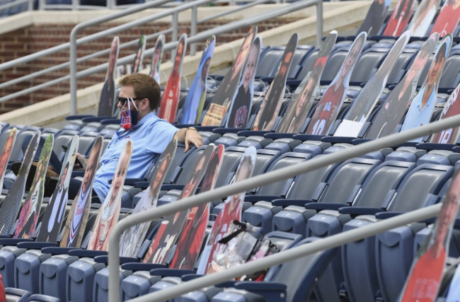 Před první polovinou školního fotbalového zápasu NCAA mezi Mississippi a Floridou v Oxfordu, 26. září, 2020, sedí fanoušek mezi lepenkovými výřezy ostatních fanoušků. / AP