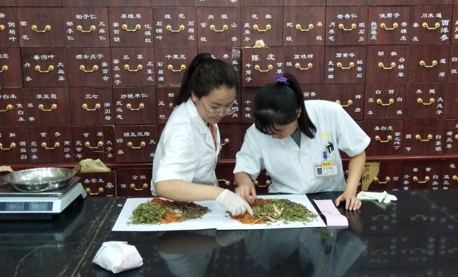 Fotografie pořízená mobilním telefonem ukazuje, jak lékárníci připravují čínskou bylinnou medicínu v obchodě s čínskou medicínou v Pekingu, hlavním městě Číny, 31. července 2019. (Xinhua / Zhang Chao)