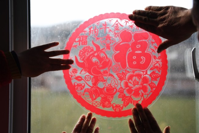 Vesničané lepí papírové ozdoby na okno svého nového domu, aby uvítali první čínský nový rok poté, co se vymanili z chudoby v Pingliang (Pching-liang) v provincii Gansu (Kan-su) na severozápadě Číny, 3. února 2021. (Xinhua / Chen Bin)