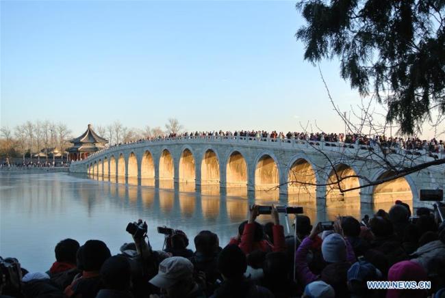 Des visiteurs admirent le paysage du Pont aux Dix-Sept Arches au Palais d'Été au moment du coucher du soleil, à Beijing, capitale de la Chine, le 6 décembre 2017. (Xinhua/Ma Zhihong)