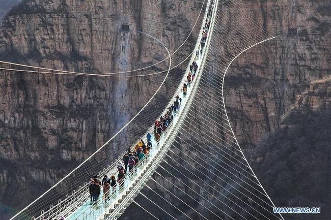 Des touristes marchent sur un pont suspendu en verre dans le site touristique de Hongyagu à Pingshan, district de la province chinoise du Hebei (nord), le 24 décembre 2017. Le pont suspendu en verre, d'une longueur de 488 mètres, a officiellement ouvert au public dimanche. (Xinhua/Liu Peiran)